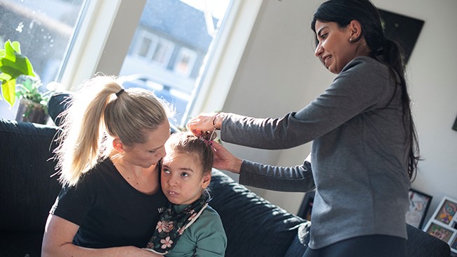 Tuva sitter i sin mammas knä medan en av assistenterna fixar hennes hår.