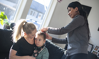 Tuva sitter i sin mammas knä medan en av assistenterna fixar hennes hår.