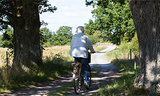 Älldre kvinna cyklar på grusväg