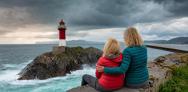 Två personer håller om varandra och tittar mot en fyr i havet