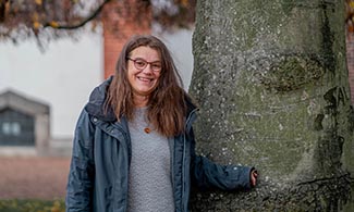 Sabina Santesson står lutad mot ett träd och tittar in i kameran.