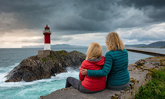 Två personer håller om varandra och tittar på en fyr i havet